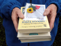 Image of older womans hands holding 4 books she has borrowed with card on top